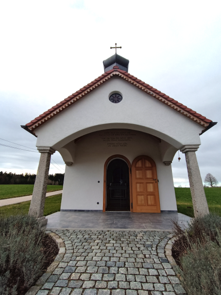 Haus mit Satteldach und Holzportal, umgeben von Rasen und Steinen.