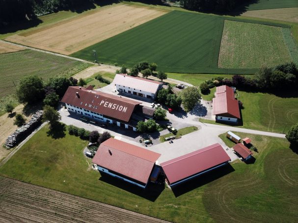 Luftaufnahme eines Bauernhofs mit mehreren Gebäuden und umliegenden Feldern.